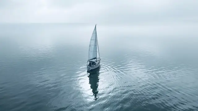 Einzelnes Segelboot auf spiegelglattem, dunstigem Wasser