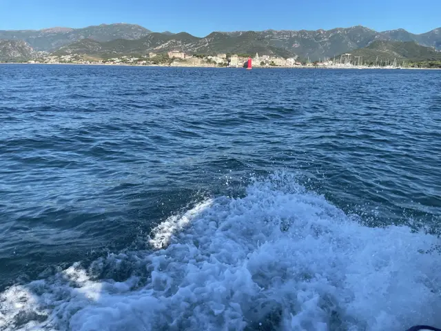 Kielwasser vor der Küste, im Hintergrund Berge und eine Stadt