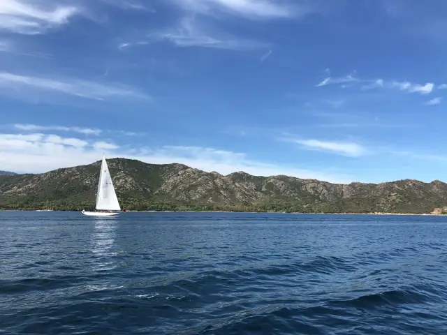 Segelboot vor grünen Hügeln unter blauem Himmel