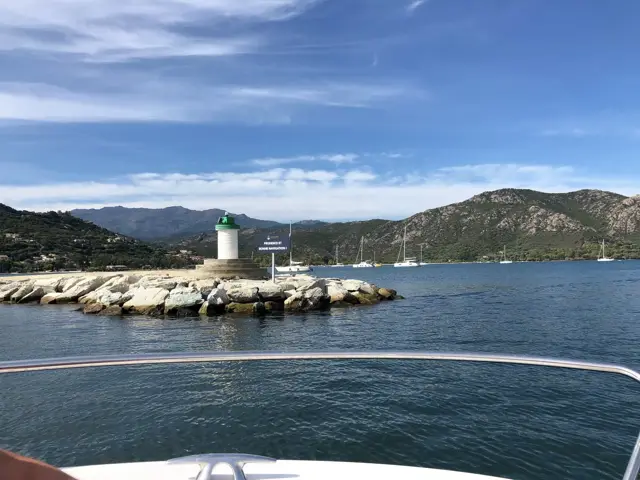 Hafeneinfahrt mit Leuchtturm auf der Mole, dahinter Berge