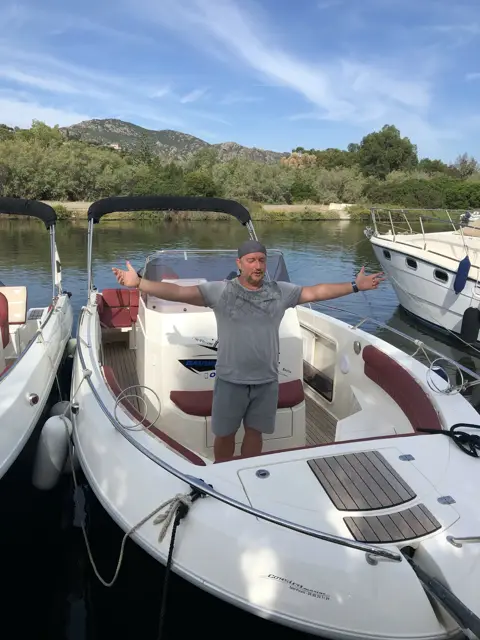 Skipper steht mit ausgebreiteten Armen im Motorboot