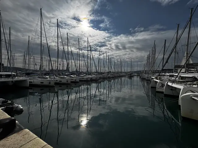 Marina mit spiegelnden Masten unter Wolken