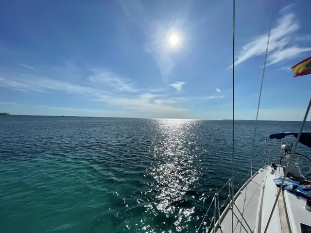 Sonne über türkisem Wasser, rechts Bordwand und spanische Flagge