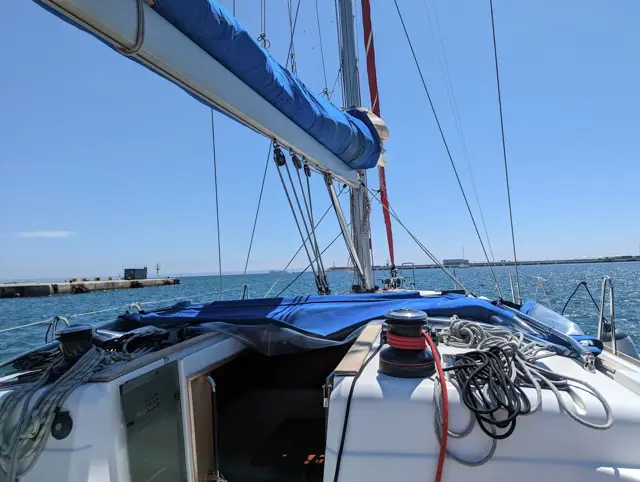 Vorschiff mit Großsegel unter Persenning, Hafen im Hintergrund